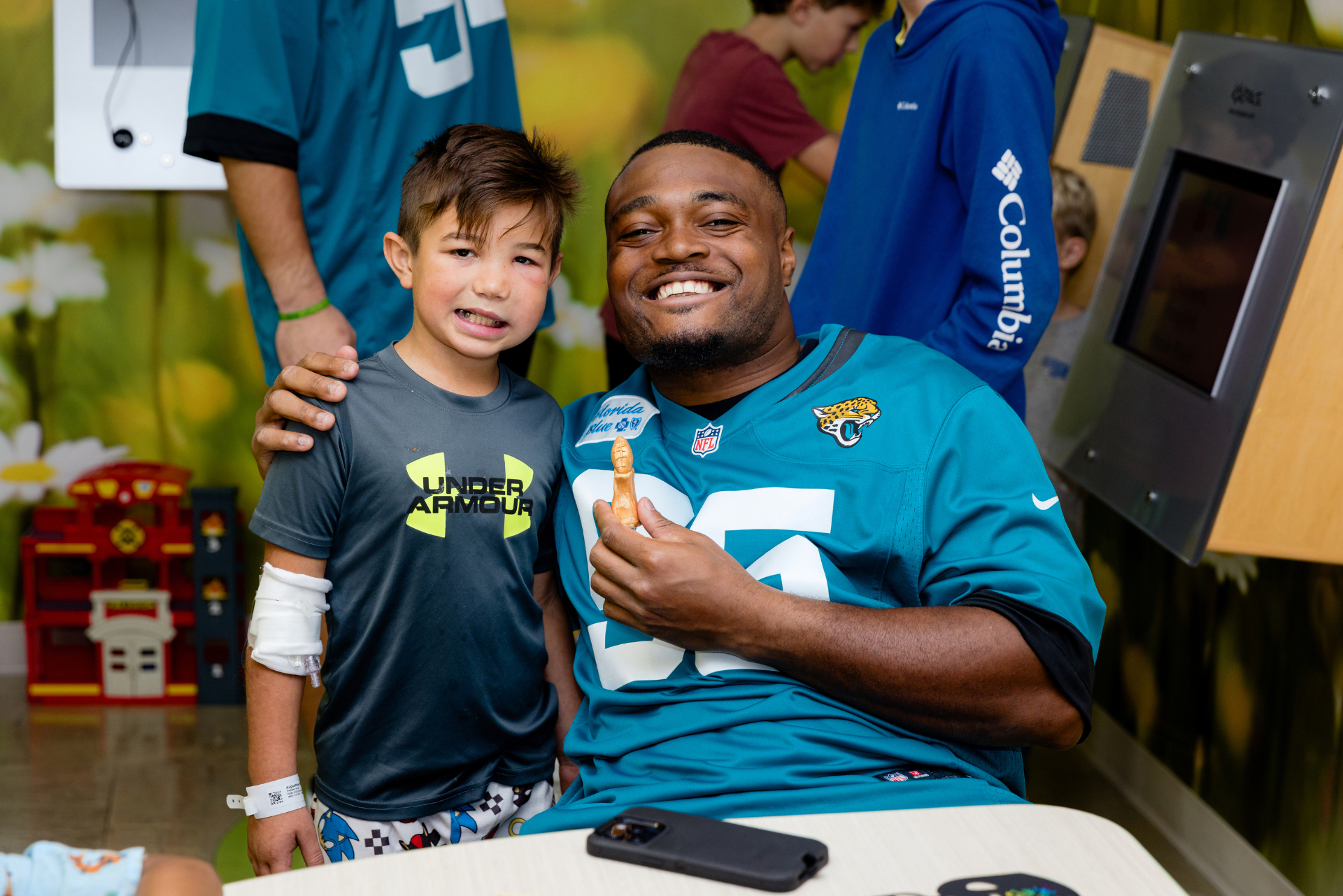 A smiling NFL player with a young hospital patient